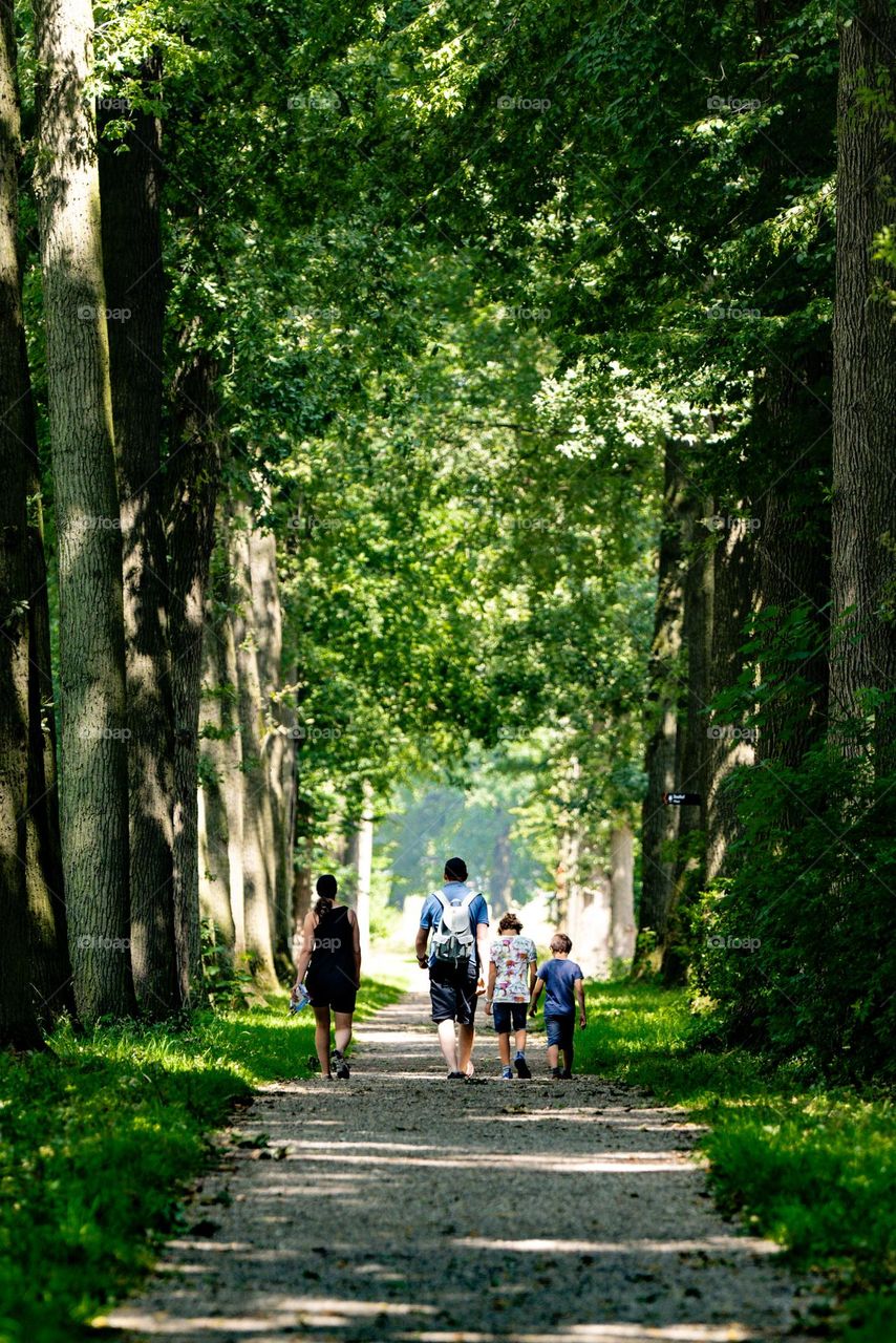 A family with parents and children hiking under trees