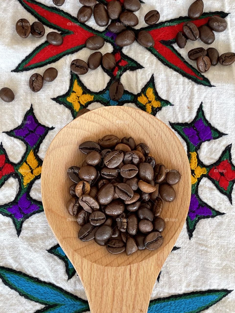 coffee theme flat lay: coffee beans on natural wooden spoon and on hand-embroidered Eritrean drape with typical ethnic embroideries