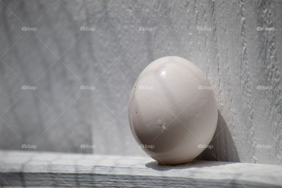Shadows holding an egg on a ledge.
