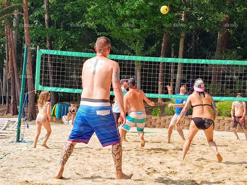Game of volleyball in the sand beside the lake with adults and children.