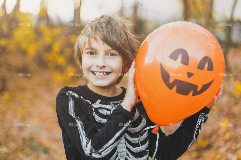 A boy in a skeleton costume holds an orange balloon with a face. Making faces, fooling around.