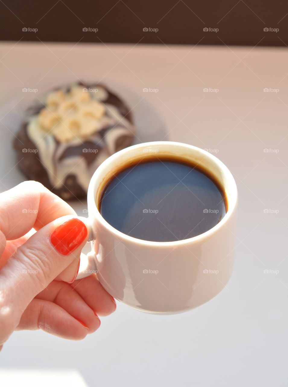 cup of coffee in the female hand and cake in sunlight on a white background