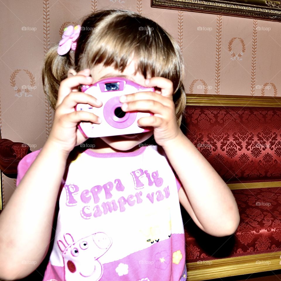 Little girl is a young photographer. girl in a pink t-shirt with a pink camera photographs