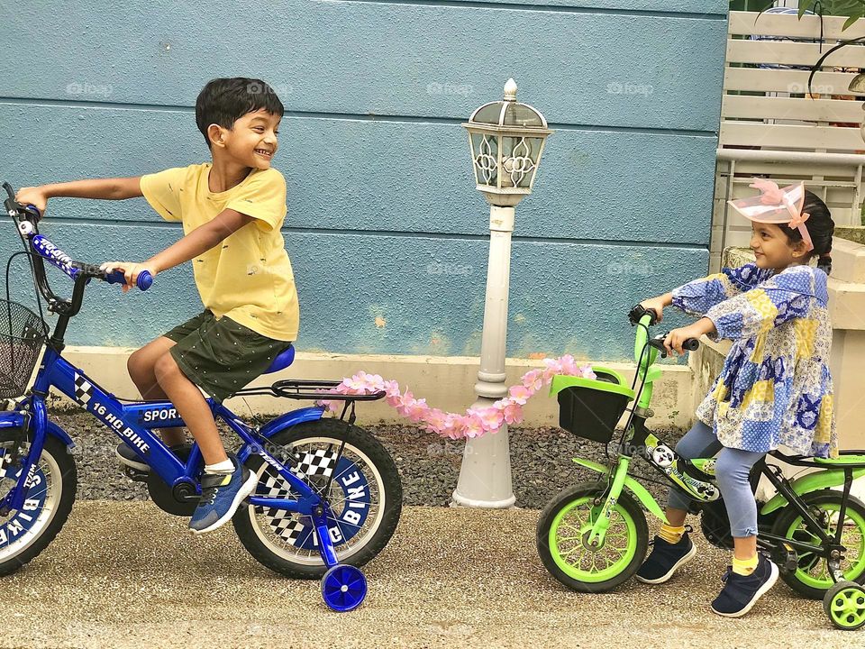 Brother and sister playing with bicycles outside the house and making fun by pulling bicycles each other with flowers garland 