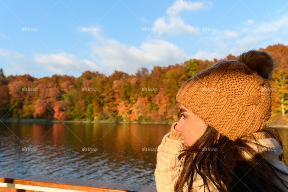 Side view of young woman on tourist boat on lake. Beautiful autumn forest on shore of lake at Plitvice lakes national park in Croatia.