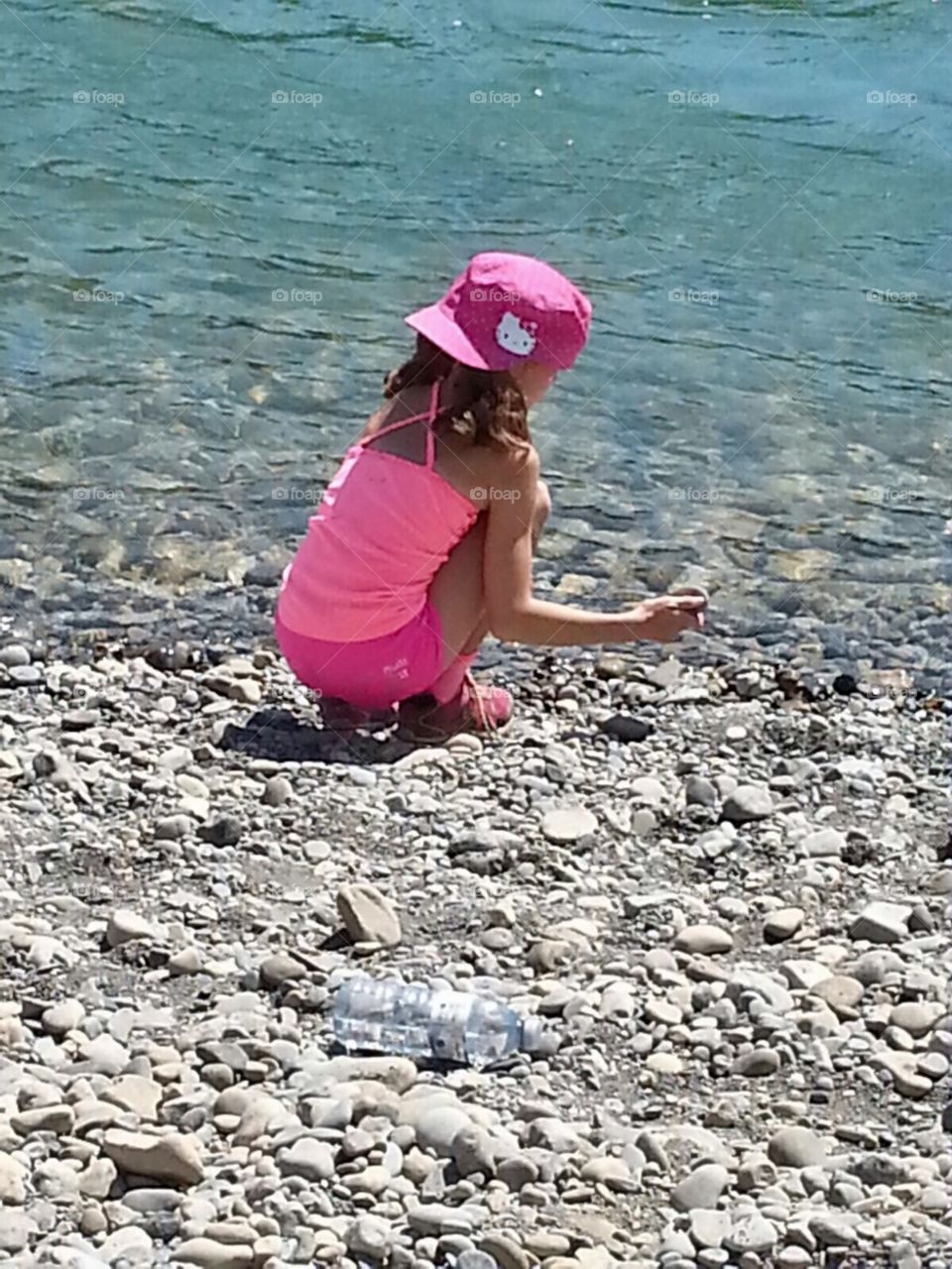 Little girl in bright pink hat and clothes playing at the river 