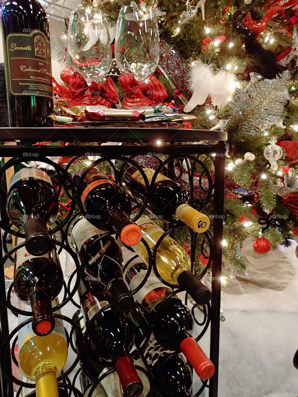 A full wine rack at the base of a Christmas tree and next to a fireplace on display for the holiday season. 