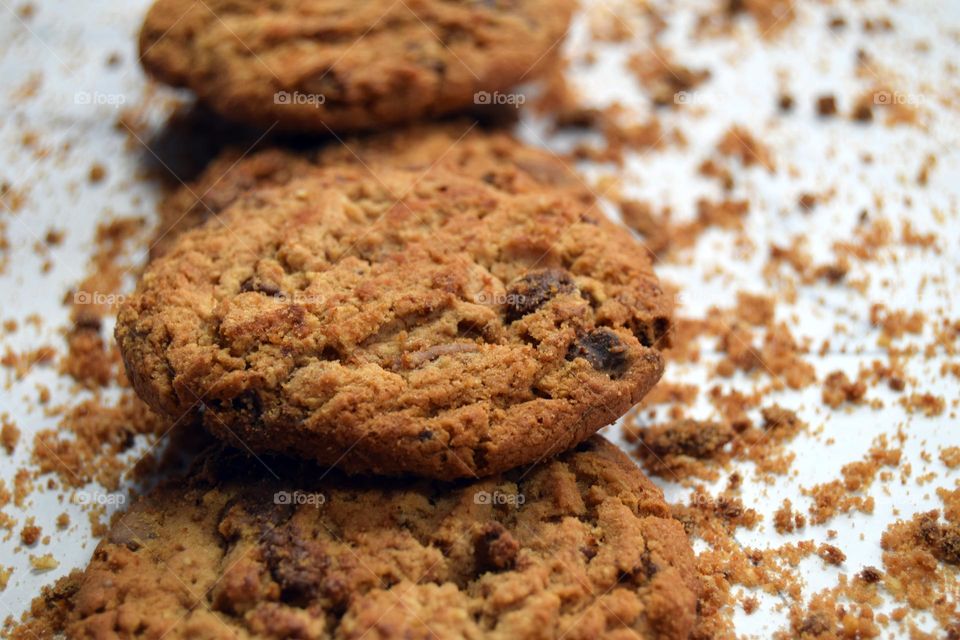 A neatly stacked vertical row of tasty golden brown chocolate chip cookies surrounded by chocolate chip cookie crumbs.