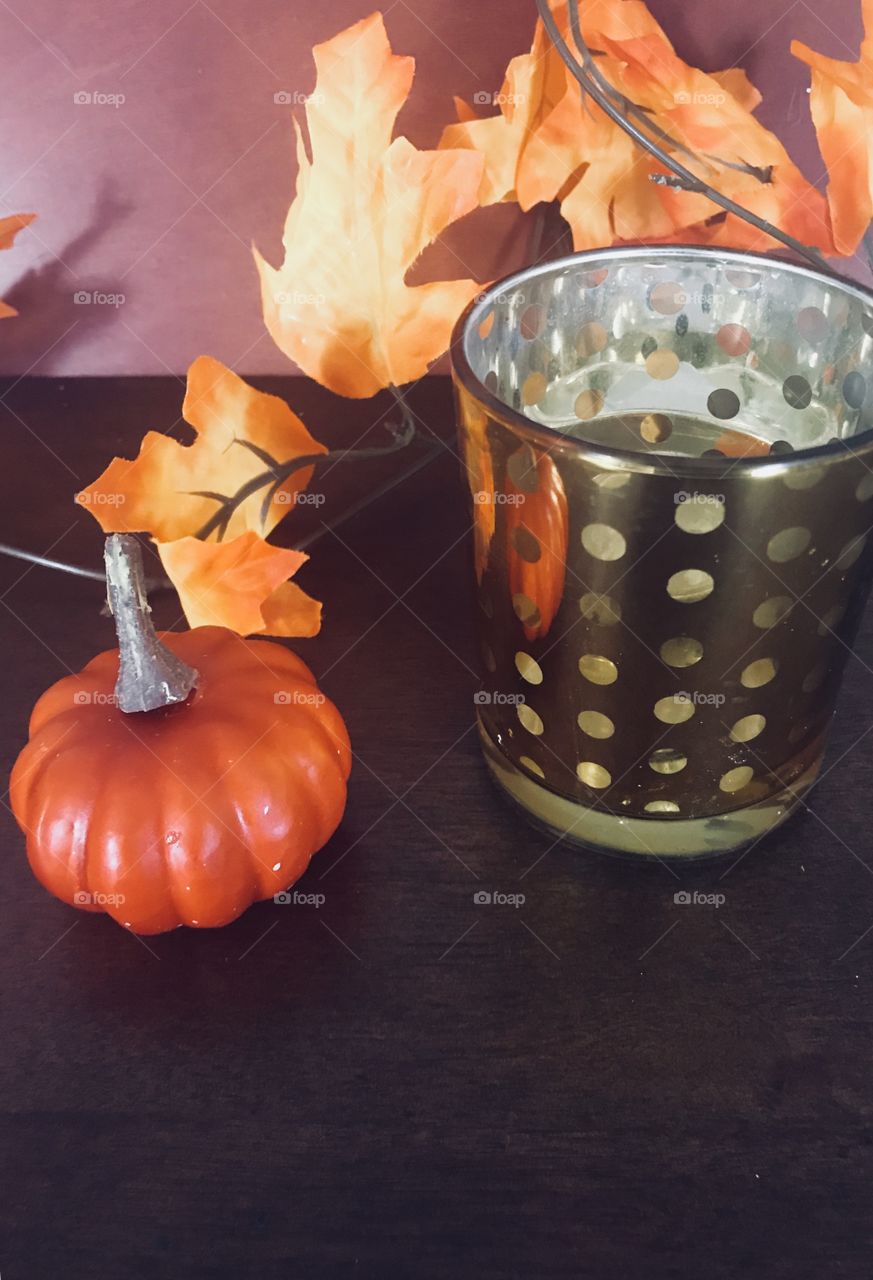 Fall table top display with a golden candle , mini orange pumpkin and colorful crisp leaves 