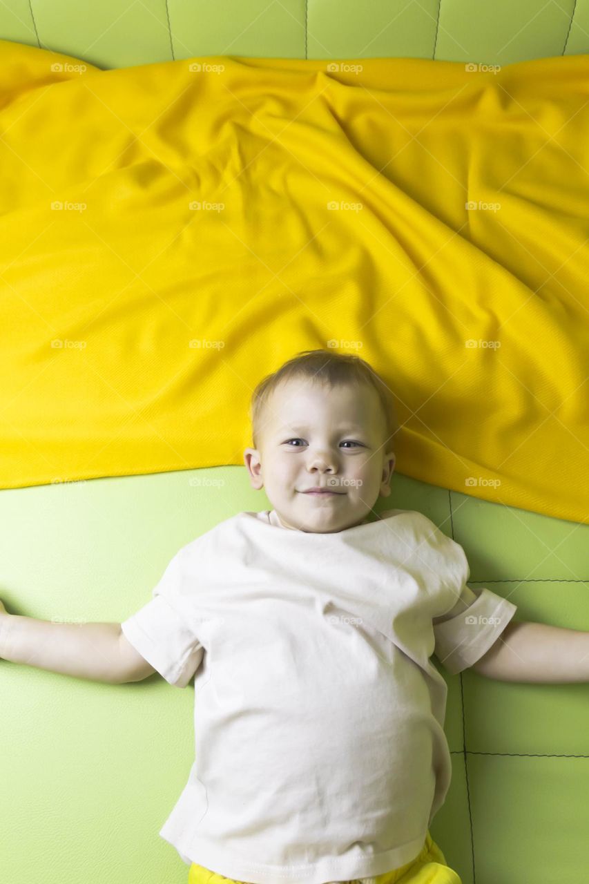 A portrait of a child sitting at home on a green sofa depicts different emotions in yellow shorts.