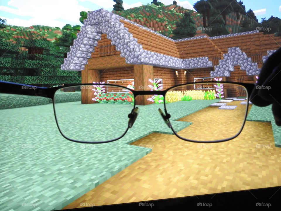 Teenager boy playing Minecraft on the gaming computer seen from his glasses close-up in a dark room.