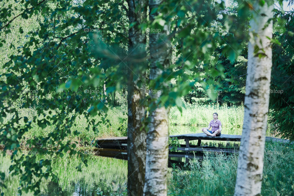 Woman sitting on a bridge over a lake, among the trees, close to nature, during summer vacations. Candid people, real moments, authentic situations