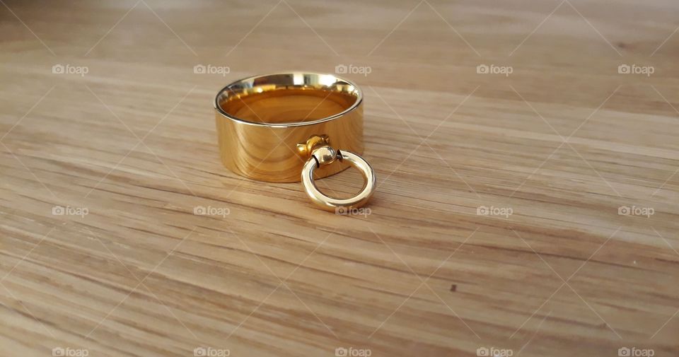 The ring of O made of gold. Presented on an oak table. A symbol of submission.