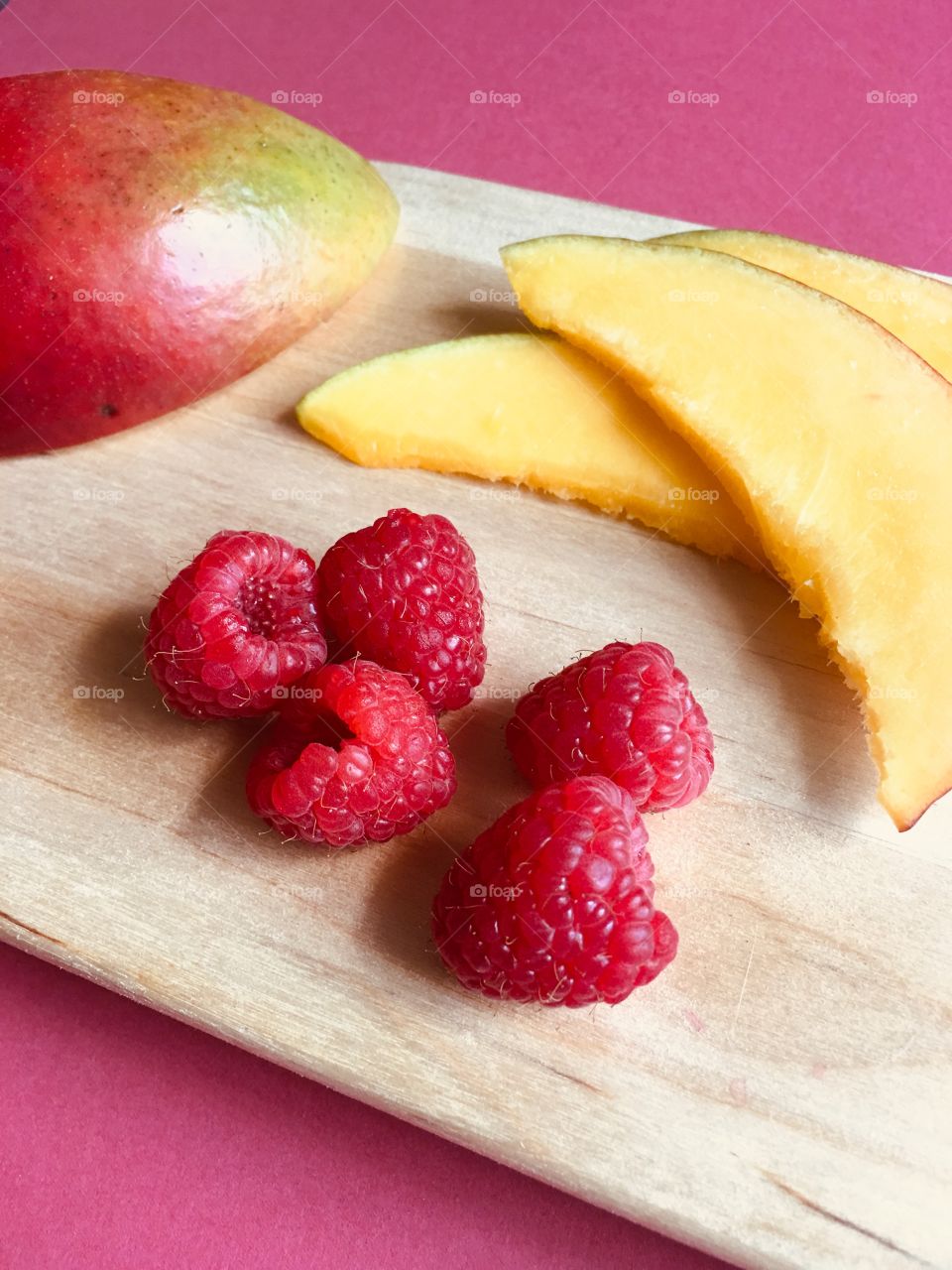 Fresh raspberries and mango slices on a wooden cutting board