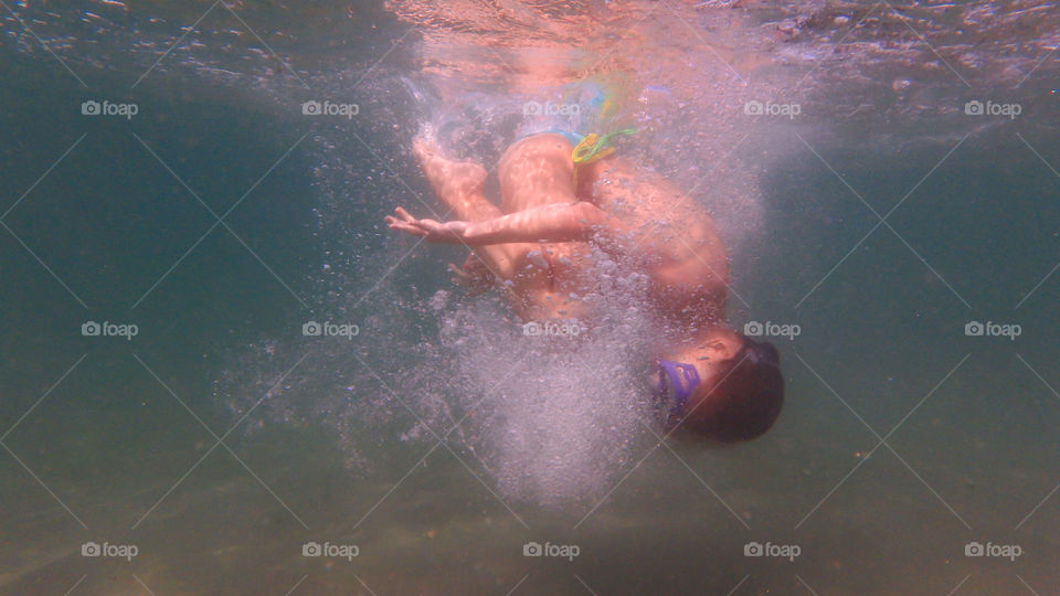 young girl spinning underwater in the sea, with bubbles all around