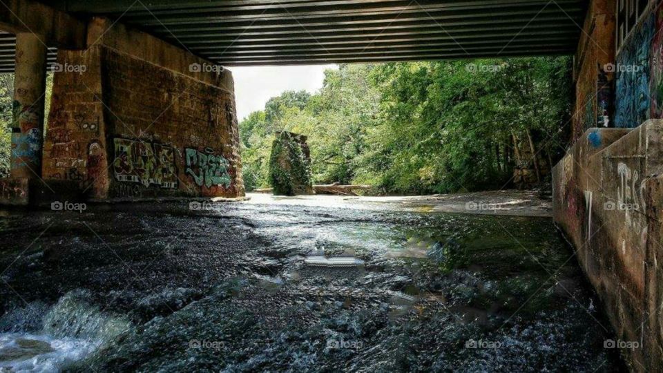 River under bridge with graffitti and old bridge support covered with vines