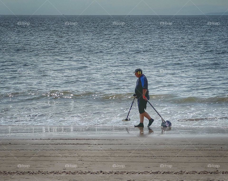 Man with a metal detector walking on a beach