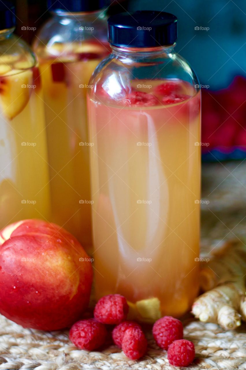 Closeup of kombucha, bottled for a second-ferment and flavored with nectarines, raspberries and slices of ginger root