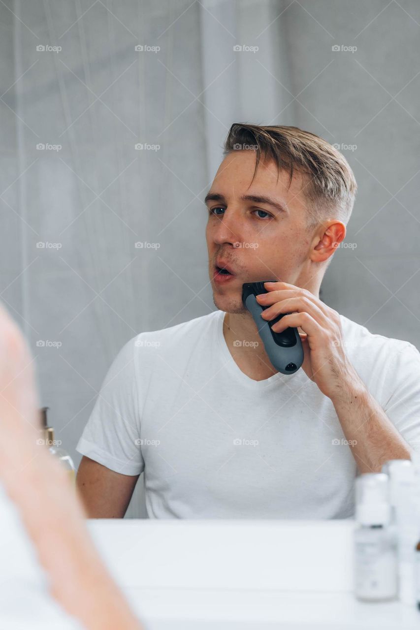 Man shaving his beard in bathroom using electric shaver 