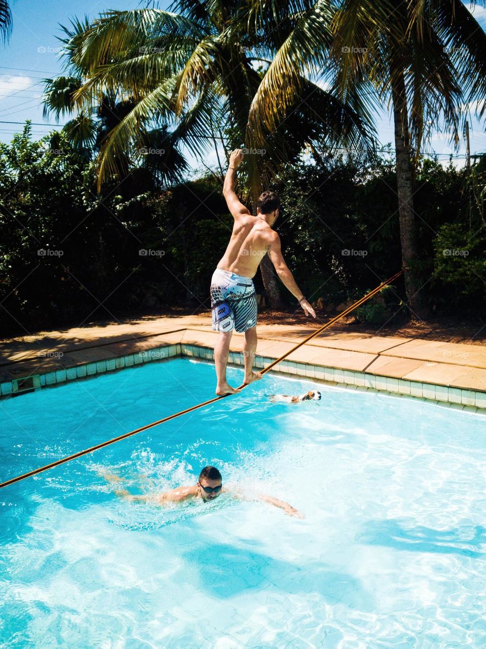 Man swimming on the pool, and another man walks on a slack line at summertime.