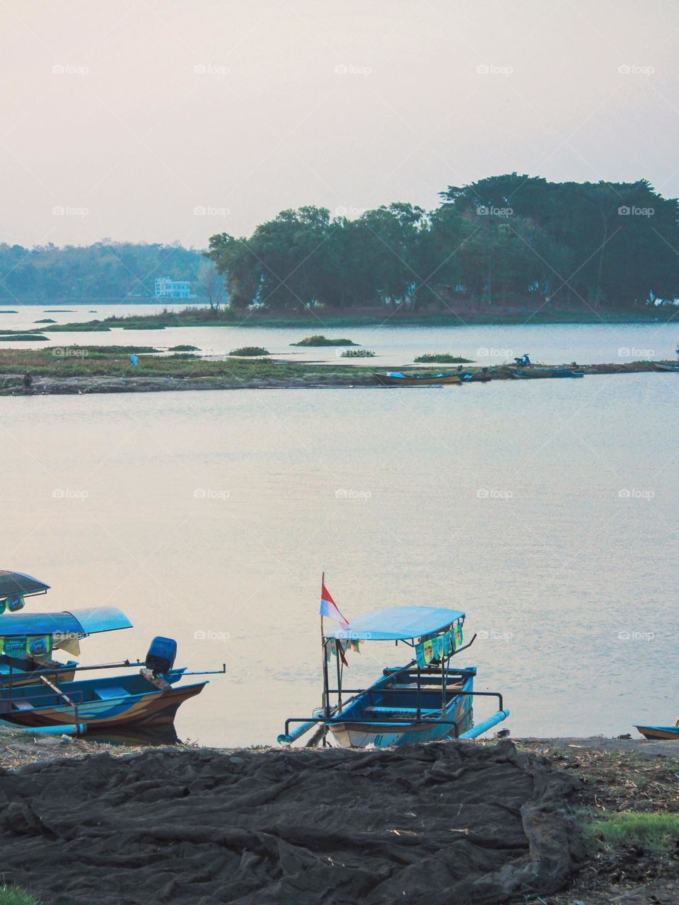 Portrait of a blue boat with a roof located on the river bank, with a calm and peaceful natural background