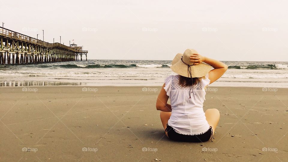 Woman Relaxing on the beach holding her hat as the wind blows