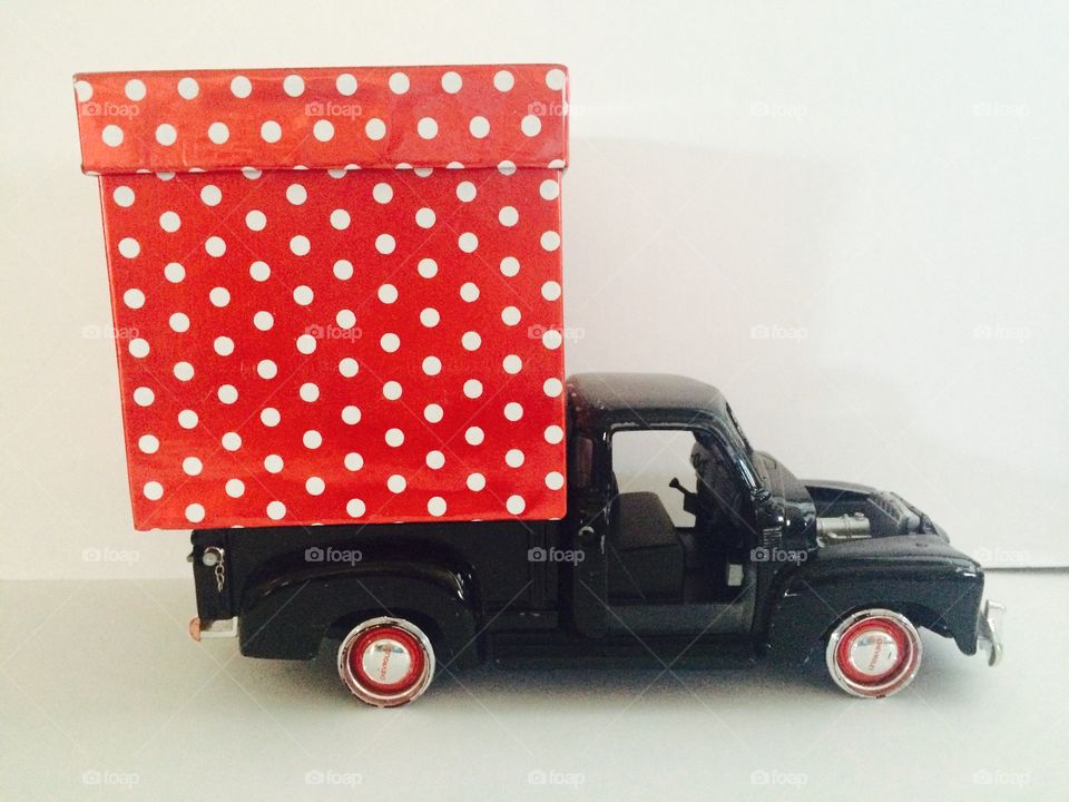Black toy truck with silver and red wheels carrying an oversized red and white gift box