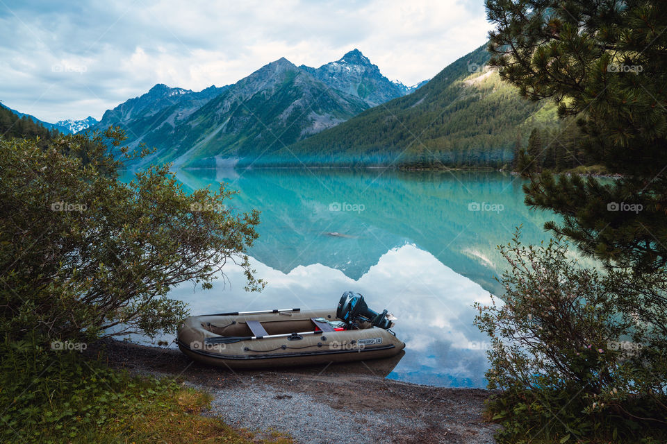 Mountain Reflection in blue lake. Inflated boat on mountain lake shore