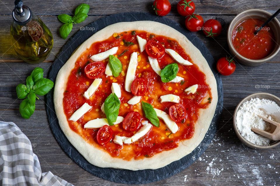 unbaked pizza with tomatoes, mozzarella cheese and basil