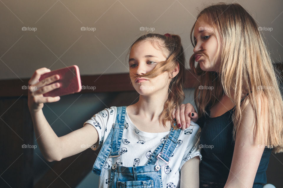 Young women taking selfie, using smartphone camera. Girls making faces, enjoying taking funny pictures together