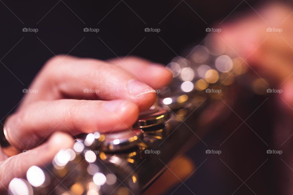 A portrait of the fingers of a flutist pressing on the flute valves of a silver flute.