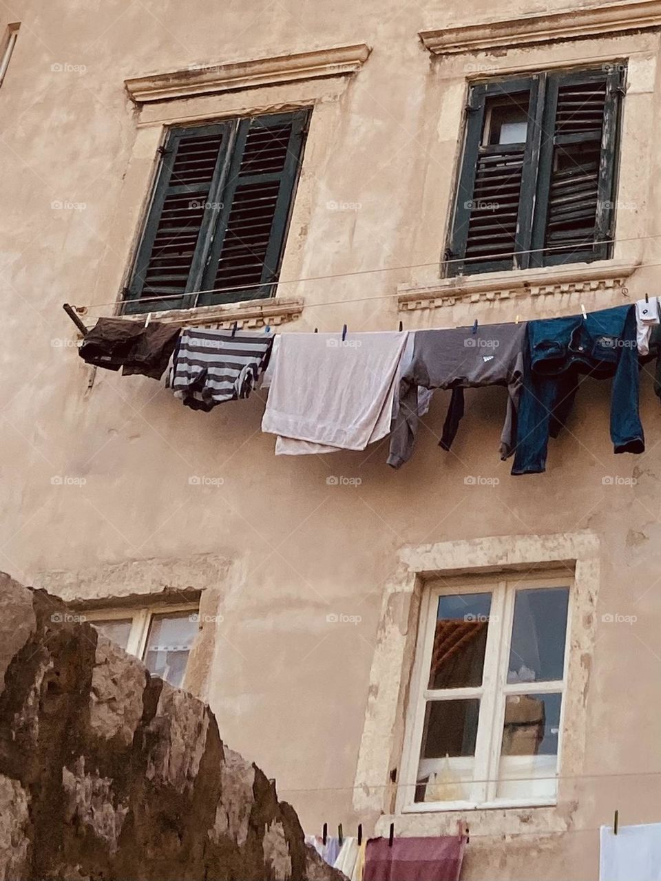 Clothes drying on a line on an old building with green wooden shutters.