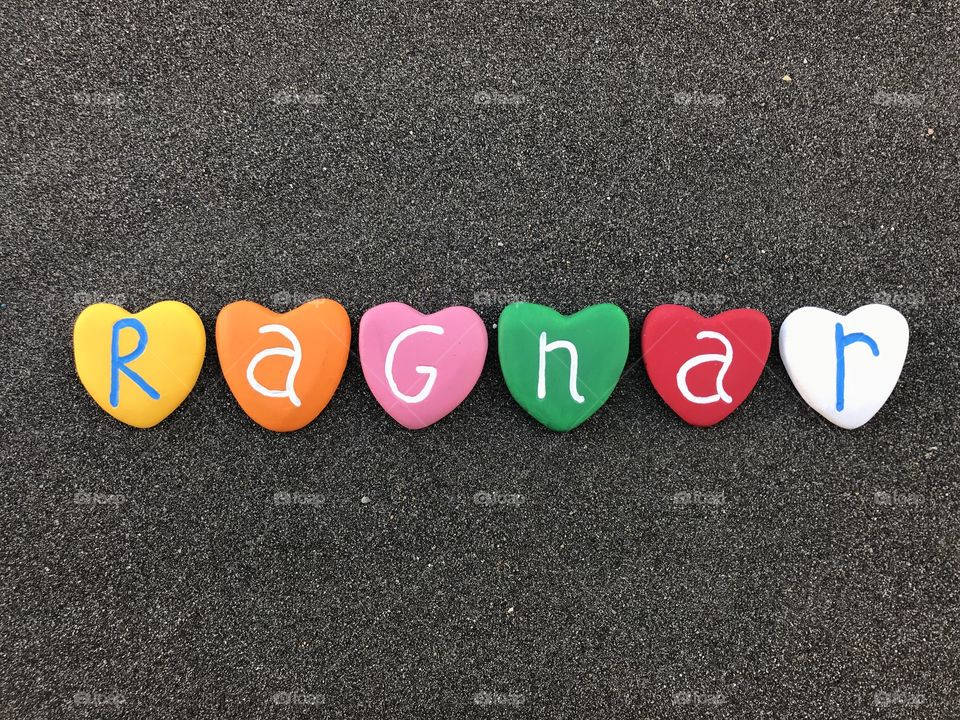 Ragnar, scandinavian masculine name and old norse origin composed with colored heart stones over black volcanic sand 





