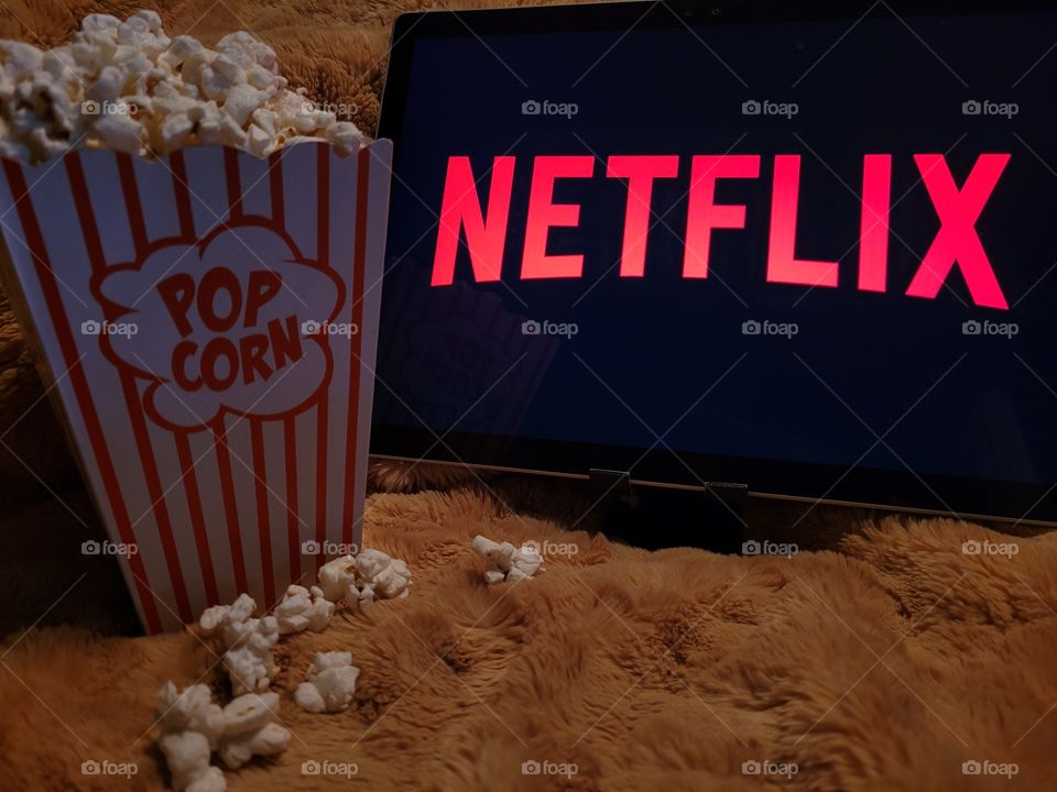 Laptop computer screen ready to watch Netflix for a fun, cozy, and relaxing night with popcorn as a snack, on soft bed blanket in dark room