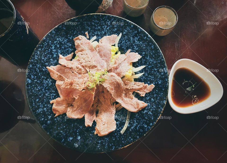 Beef Tataki a Japanese Cuisine on a blue serving plate with sauce on brown table. 
