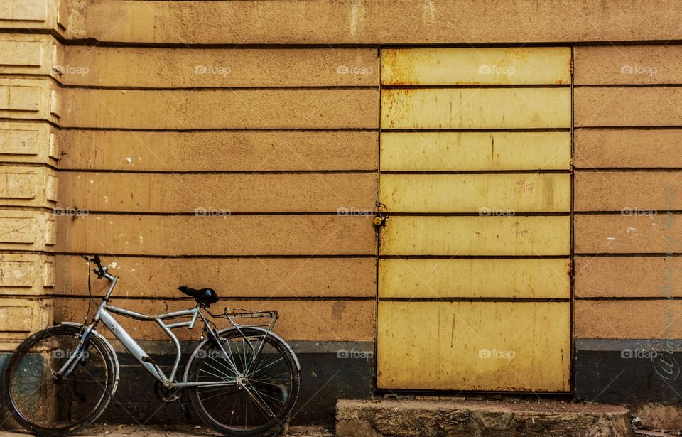 silver colored old bicycle parked against yellow wall