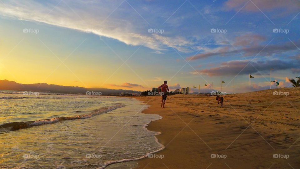 Man running with dog by the beach