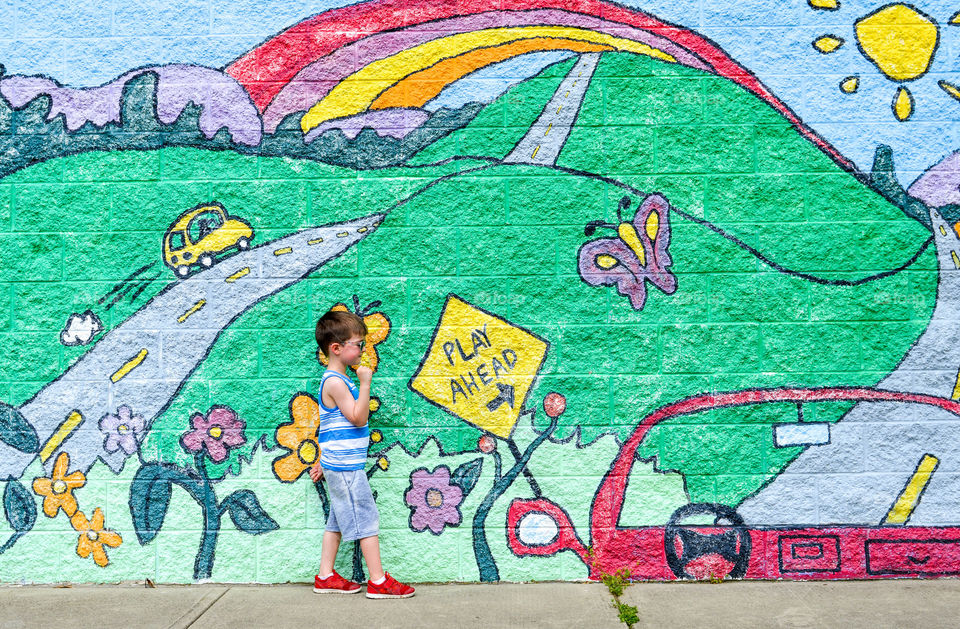 Young boy walking in front of a colorful playground mural in the summer