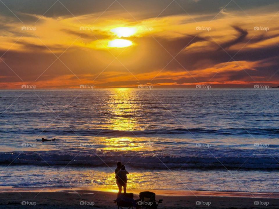 A couple embrace on a beach while admiring a beautiful golden sunset in San Diego