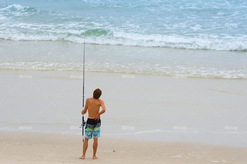 a young man fishing in the beautiful blue ocean from the sandy beach