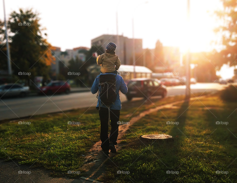 Father and son hiking together with a backpack through the autumn city during the golden hour 