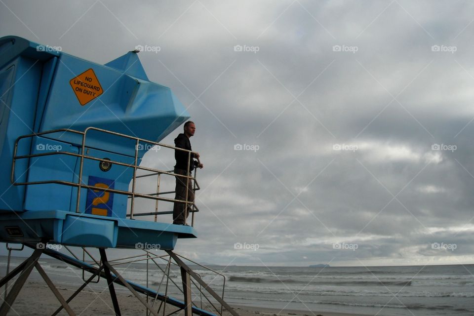 Man standing on lifeguard cab near sea