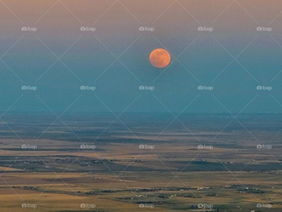 A full moon rising appears red as it comes up over the Colorado plains