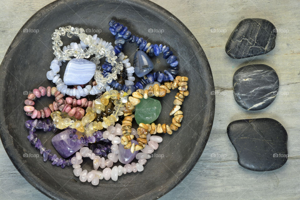 gemstones in a black bowl with zen stones on a grey wooden background