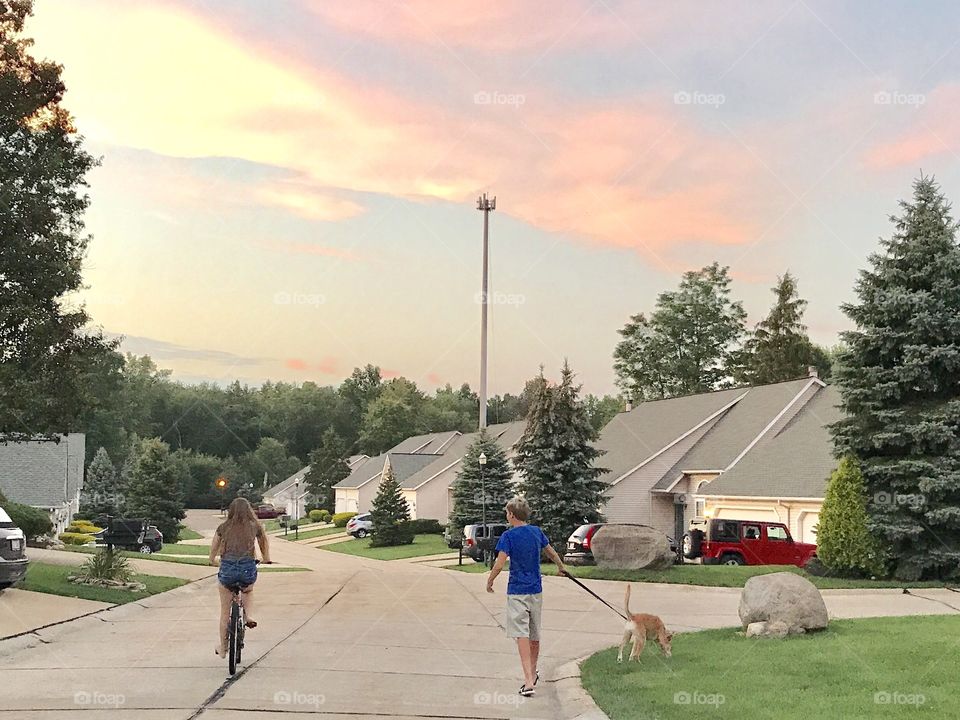 Girl riding bicycle on road and a man with dog at town