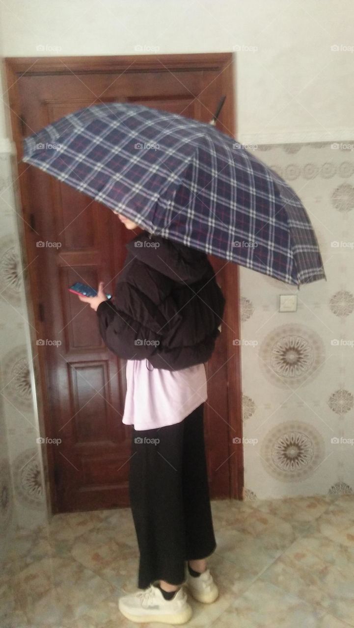 a girl under umbrella holding its phone.