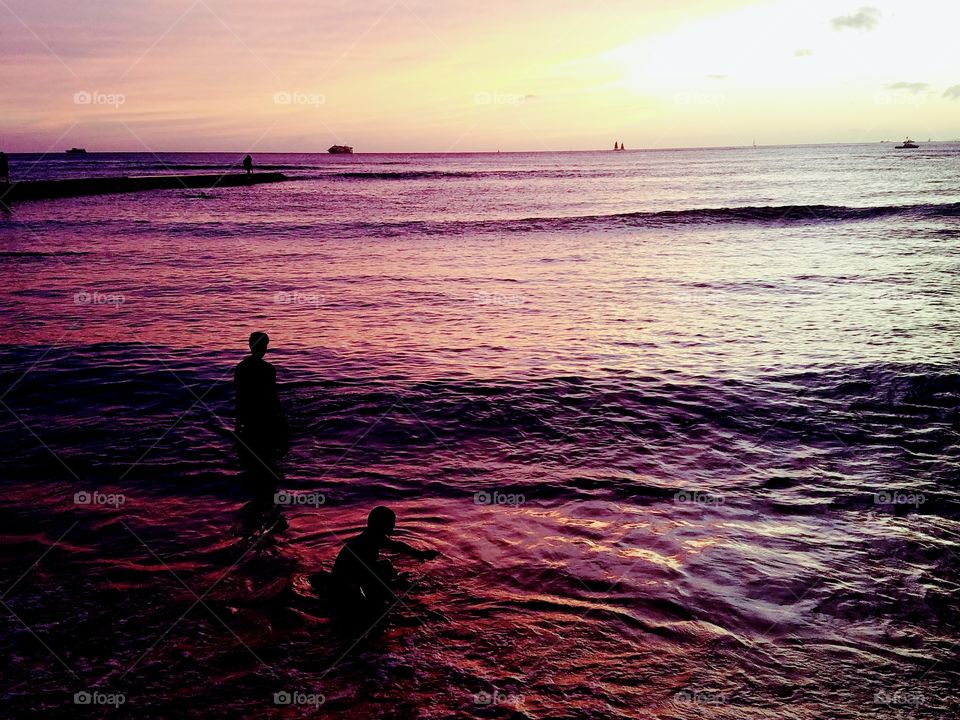 people play on the shoreline as the sunsets over Waikiki Beach