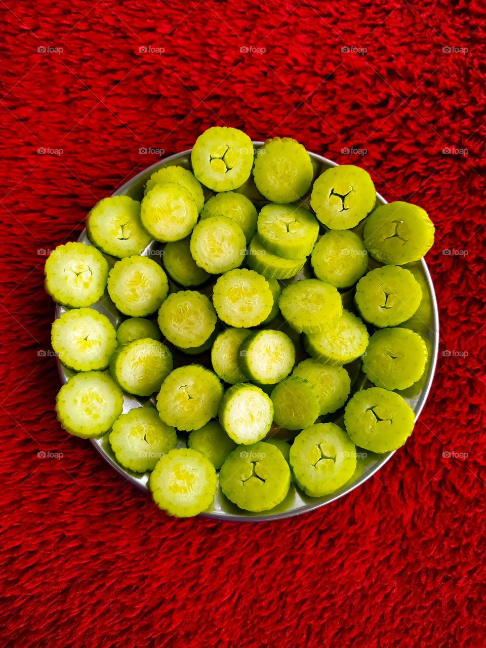 Fresh cucumber slices in steel plate on red background