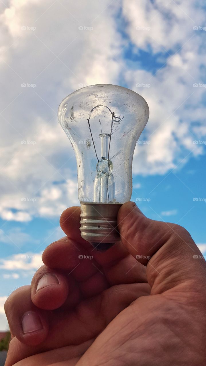 Light bulb in hand against sky background
