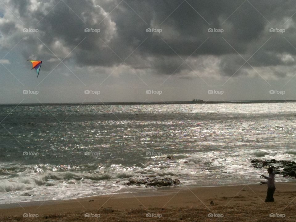Flying a bright kite on a blustery Devon beach against the grey sky. The sun twinkling on the ocean. 